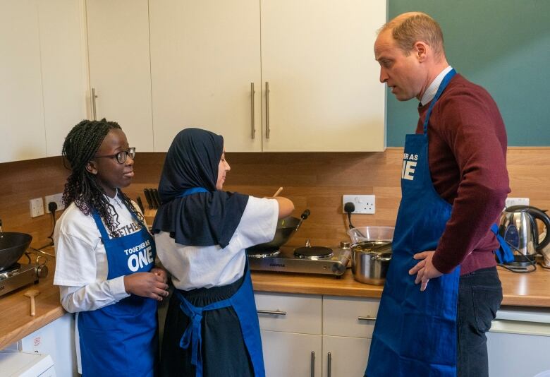 An adult talks with young people in a kitchen.