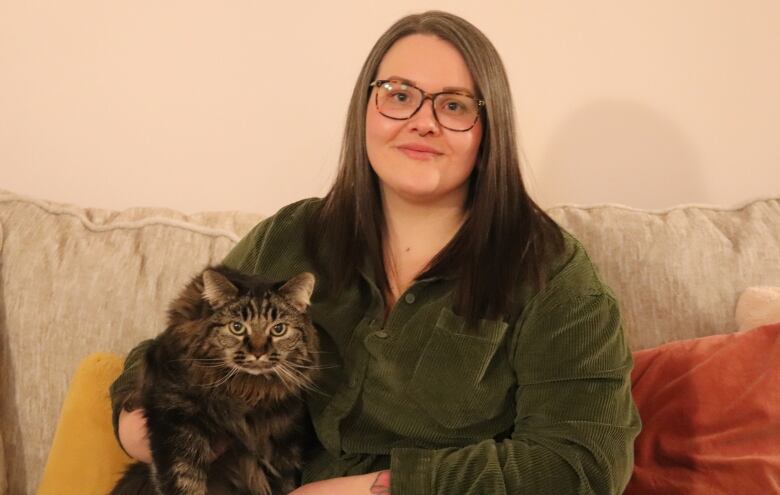 A woman holds a brown and black cat well sitting on a tan sofa