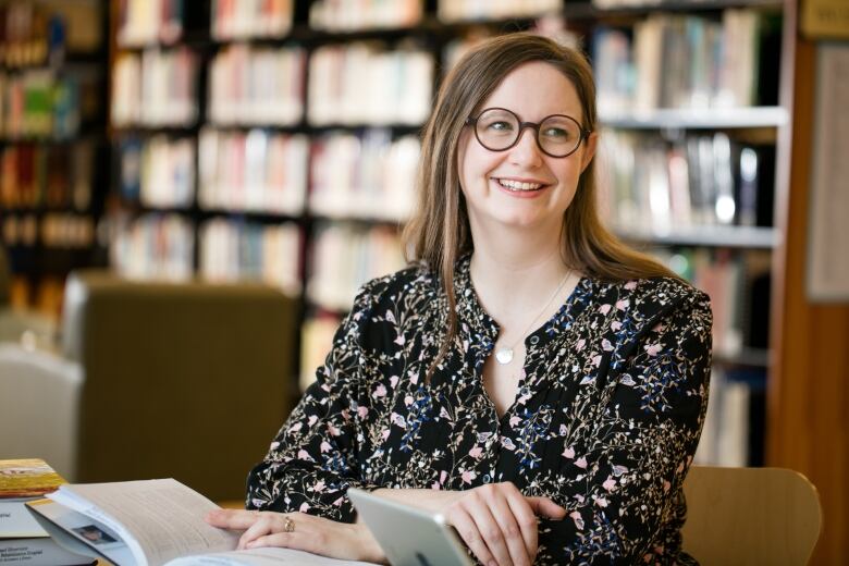 Dr. Penner is shown smiling, wearing glasses and a flowered blouse, in front of a wall of books.