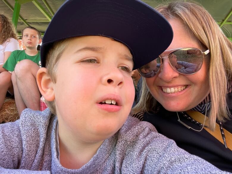 Ewan is shown in the foreground wearing a baseball cap, with his mother, Stephanie, close beside him, wearing sunglasses.