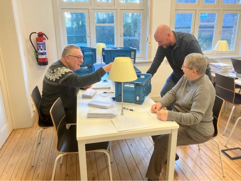 three people at a table, with stacks of envelopes and stationary around them.