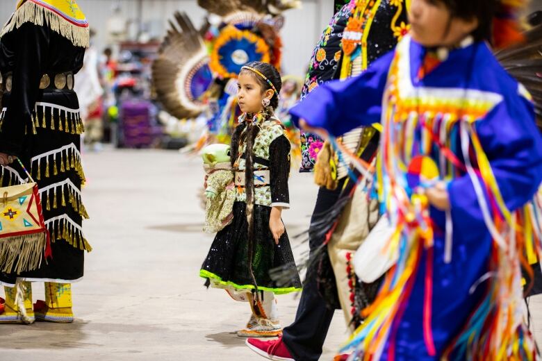 A girl dressed in powwow regalia holds a baby yoda.