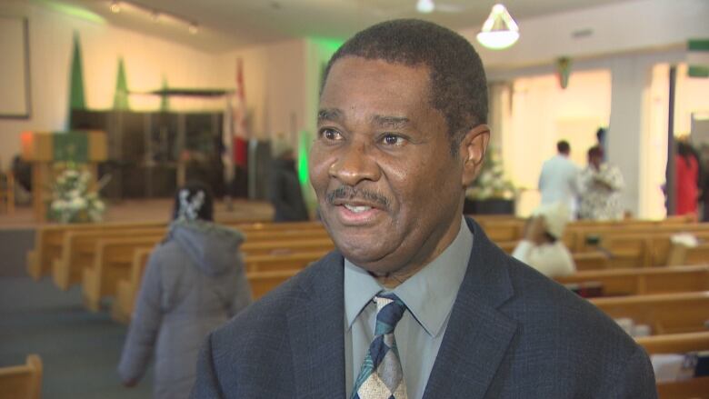 A pastor standing in a church, while the parishioners behind him prepare to head home.