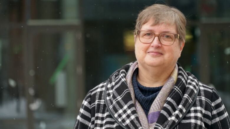 A woman wearing a coat and scarf poses for a photo outside while it's snowing.