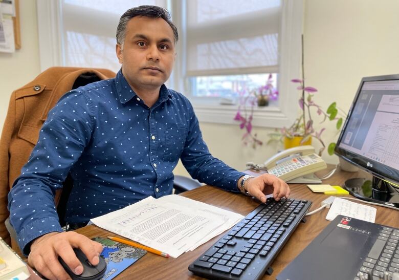 A man in a polka-dot dark blue shirt sits at a computer, looking toward the camera.