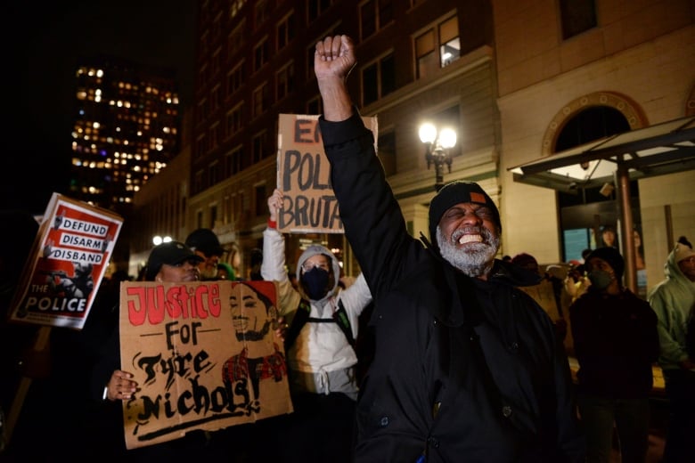 A man with his fist raised is pictured in a dark street, followed by several people holding signs.