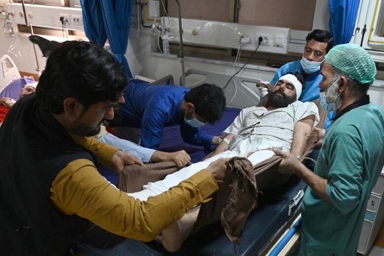 A man with a bandage on his head lies on a stretcher in a hospital as medical staff treat him.