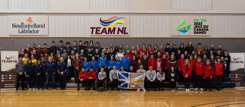 A panoramic photo of athletes standing on bleachers. A Newfoundland and Labrador flag with a number of signatures on it is being held in the middle of the photo by Premier Andrew Furey.