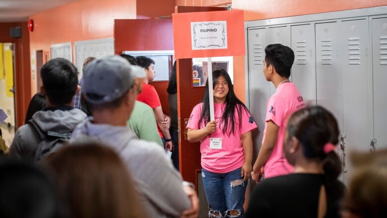 Students and parents gather in a school hallway around a volunteer who is holding a sign that says Filipino.