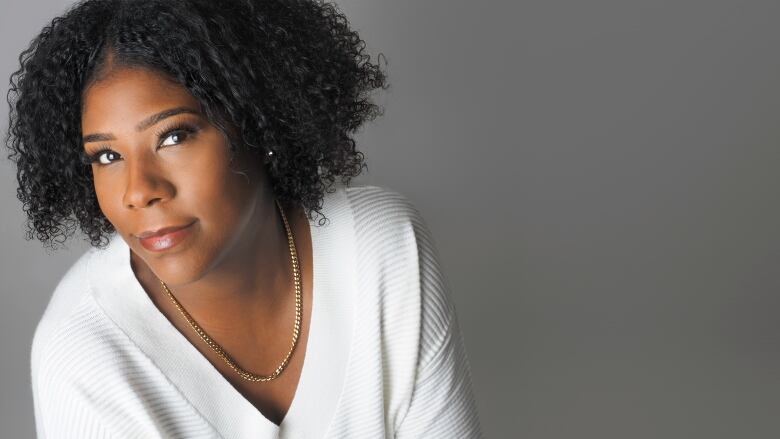 A head-and-shoulders shot of a young Black woman wearing a simple gold chain and a white sweater.