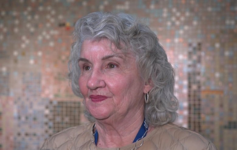 A woman stands in front of a microphone answering questions from a reporter.