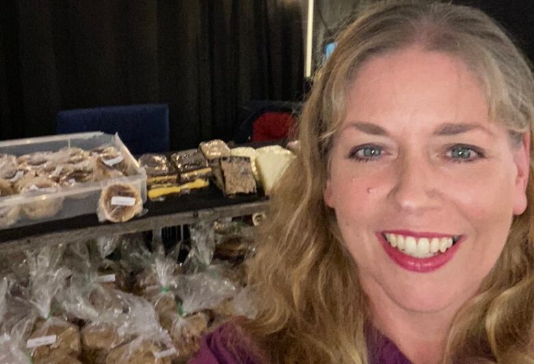 Woman with long curly blonde hair smiles in front of an array of baked goods. 