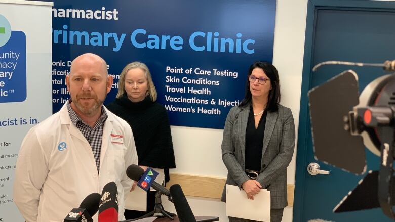 A bald man speaks as a podium while two women stand behind him.