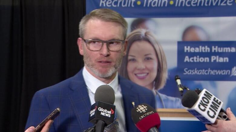 A man clad in a blue suit speaks to microphones.