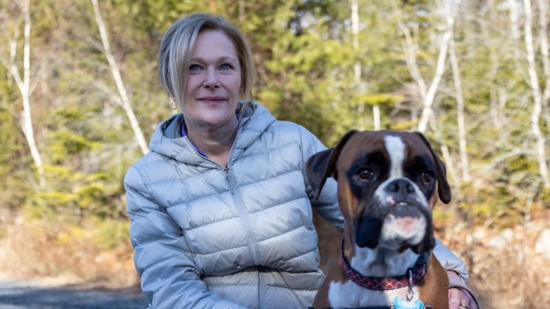 A woman standing in front of trees hugging a dog.