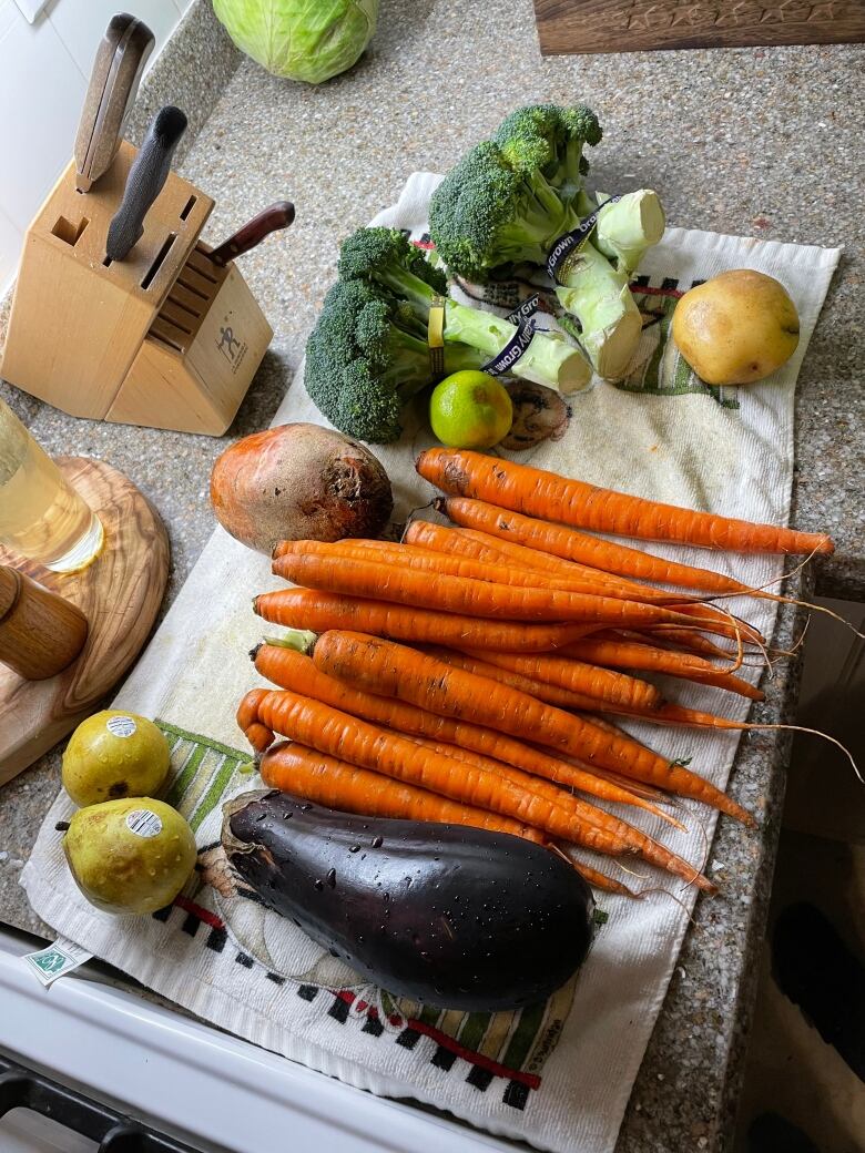 A selection of washed veggies including carrots, eggplant, broccoli and potatoes sit on a kitchen counter.