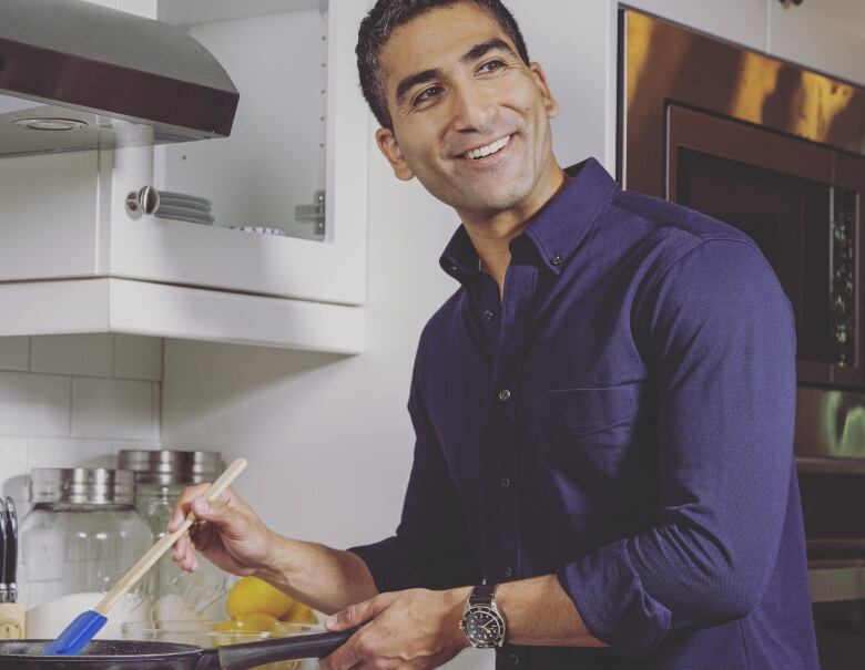 A man smiles as he stirs food in a frying pan over a stove. 