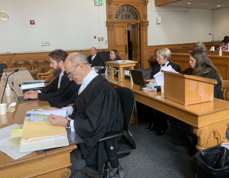 Three pairs of people wearing lawyers' robes sit in a court room.