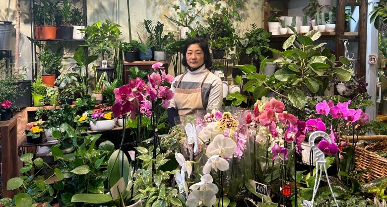 A woman in an apron, surrounded by lush plants and flowers.