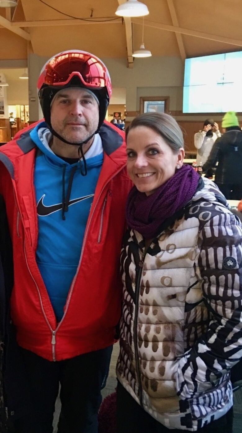 A man in a ski suit and helmet beside a much shorter woman.