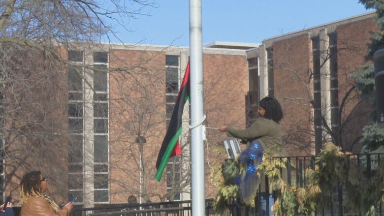 A woman raises a flag up the pole. 