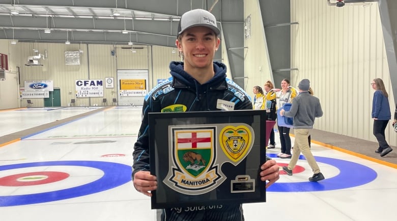 A curler stands with a plaque after a victory.