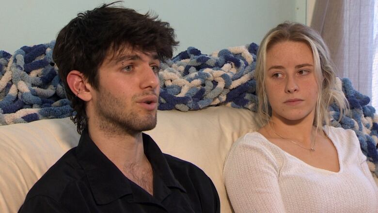 Two young adults sit on a couch. 