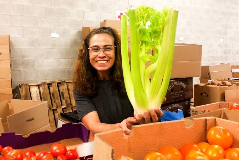 A woman with glasses holds up a bunch of misshapen celery.