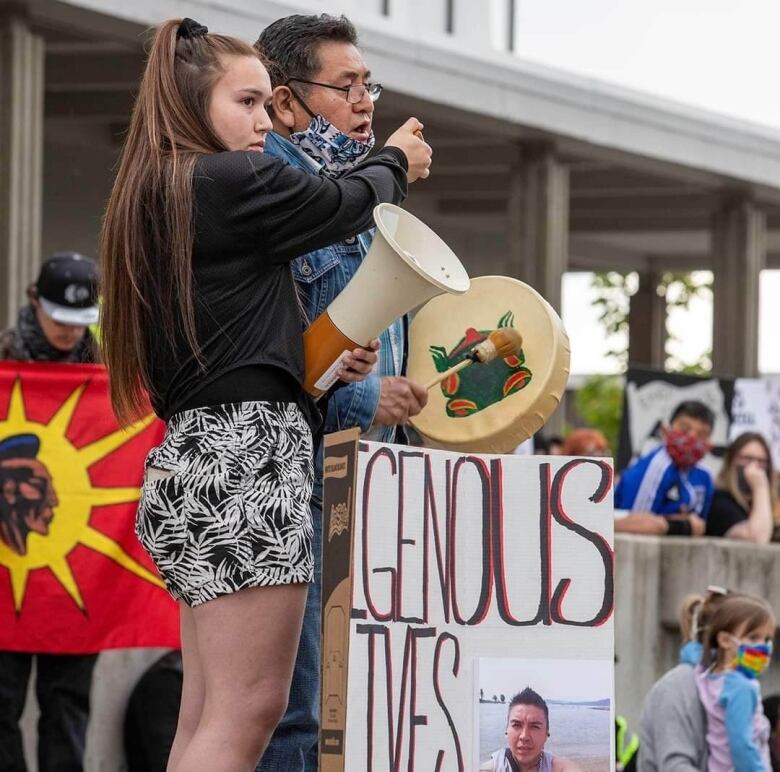 A teenaged girl holds up a microphone for a speaker at a rally.