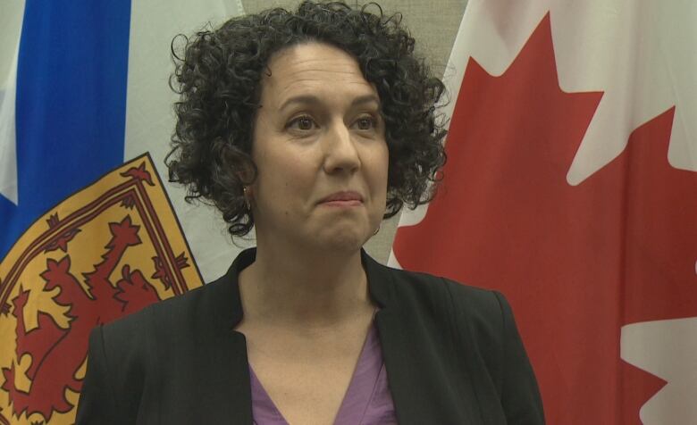 A woman with black hair stands in front of the Canada and Nova Scotia flags.