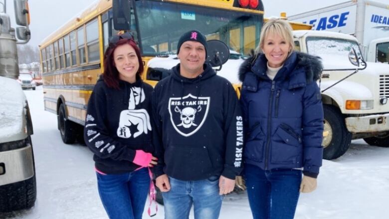 Three people standing in front of a school bus in the winter.