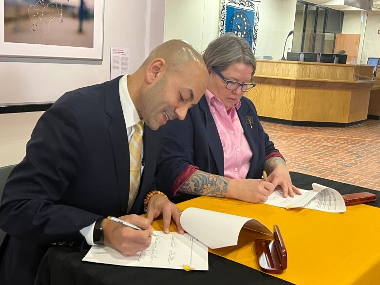 A man in a suit and a woman in a blazer and pink button up sign documents at a table. 