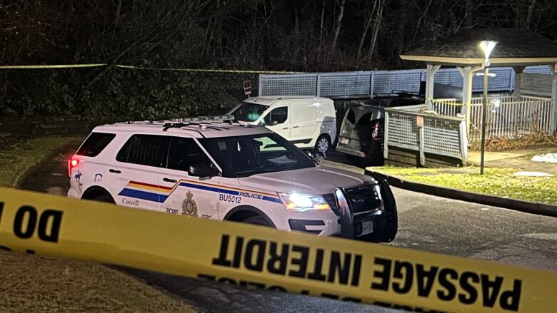 Police tape and three vehicles, including a police SUV, block off the entrance to an underground parkade during the night at a townhouse complex.