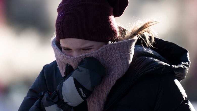 Wearing a tuque, a woman is outside wearing a puffy jacket and scarf.