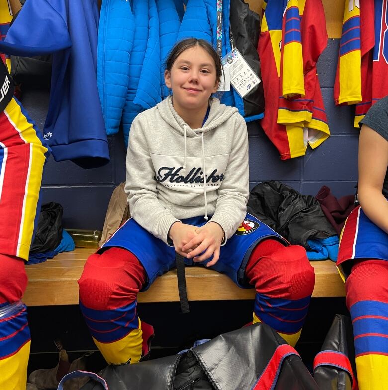 Girl in bright hockey equipment in dressing room.