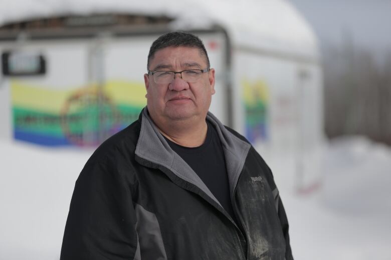 A man dressed in a black partially zipped jacket standing outside during the winter on Peguis First Nation. 