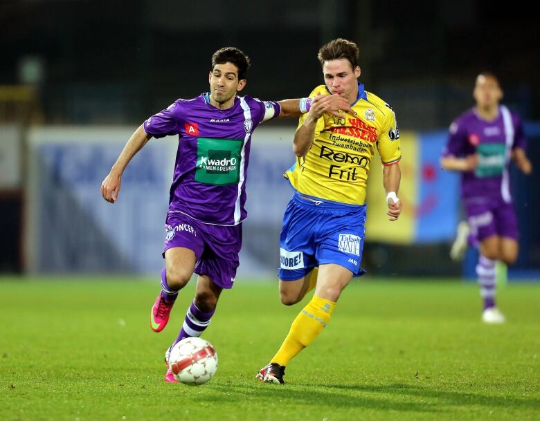 Two soccer players battle over the ball.