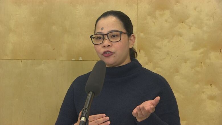 A woman with glasses and her hair pulled back speaks into a microphone.