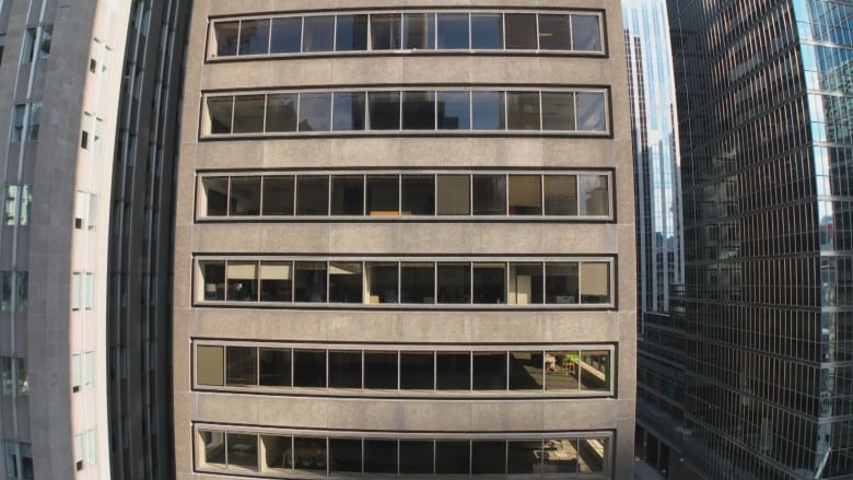 A plain looking mid size tower in downtown Toronto with a beige exterior.  The picture taken by a drone in mid air shows several empty offices.      