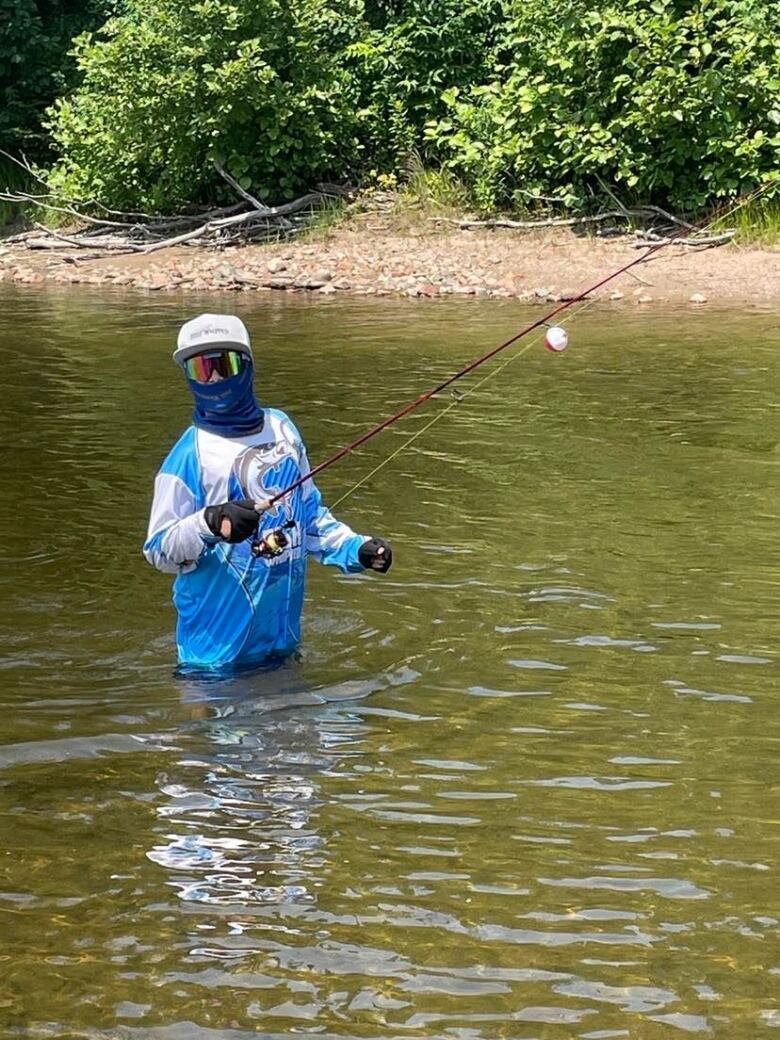 A boy in a river while holding a fishing rod.