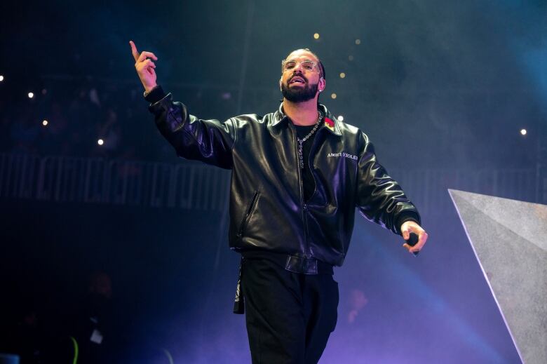 Rapper Drake performs on a blue lit stage wearing all black with a microphone in his hand