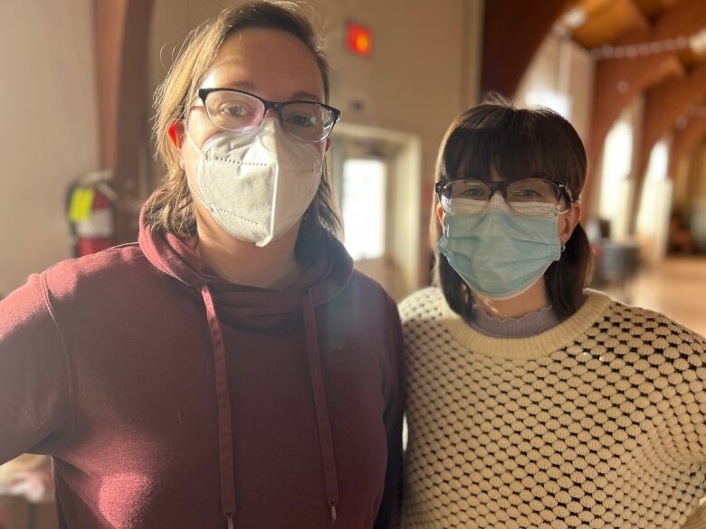 Two people stand next each other wearing face masks.