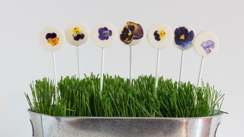 Edible floral pastry pops on sticks rise up above a fake grass grass arrangement.