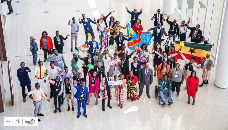 A group of people look up from the floor for an overhead shot. There is a Zambian flag being held up by two of the people.