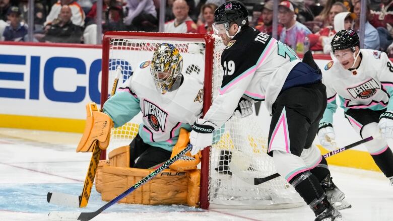 A male ice hockey player shoots the puck as the opposing goaltender looks to make a save on his knees.