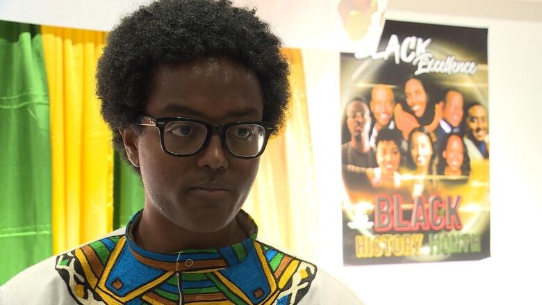 A Black man wearing glasses and a colourful shirt poses for a photo.