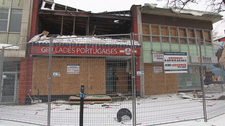 A charred and boarded up grocery store with a red sign reading 