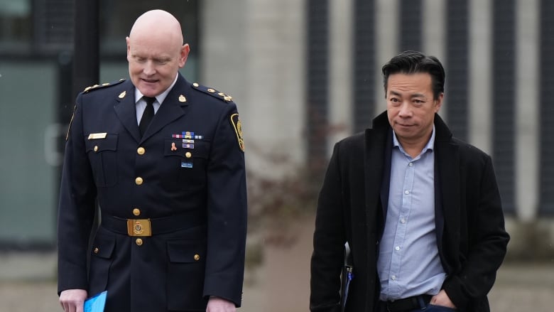 A police chief in uniform walks alongside the Vancouver mayor who's wearing a blue button up shirt and a black wool jacket.