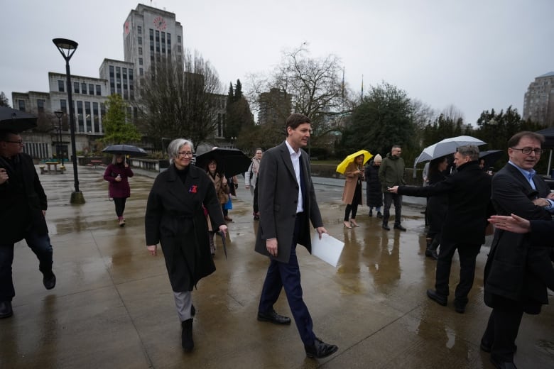 A group of provincial officials arrive at a news conference in Vancouver. Tall, lanky Premier David Eby is in the centre wearing a grey wool jacket.