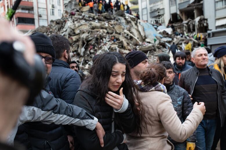 A dark-haired woman is shown in the foreground as several people look on amid a pile of rubble.